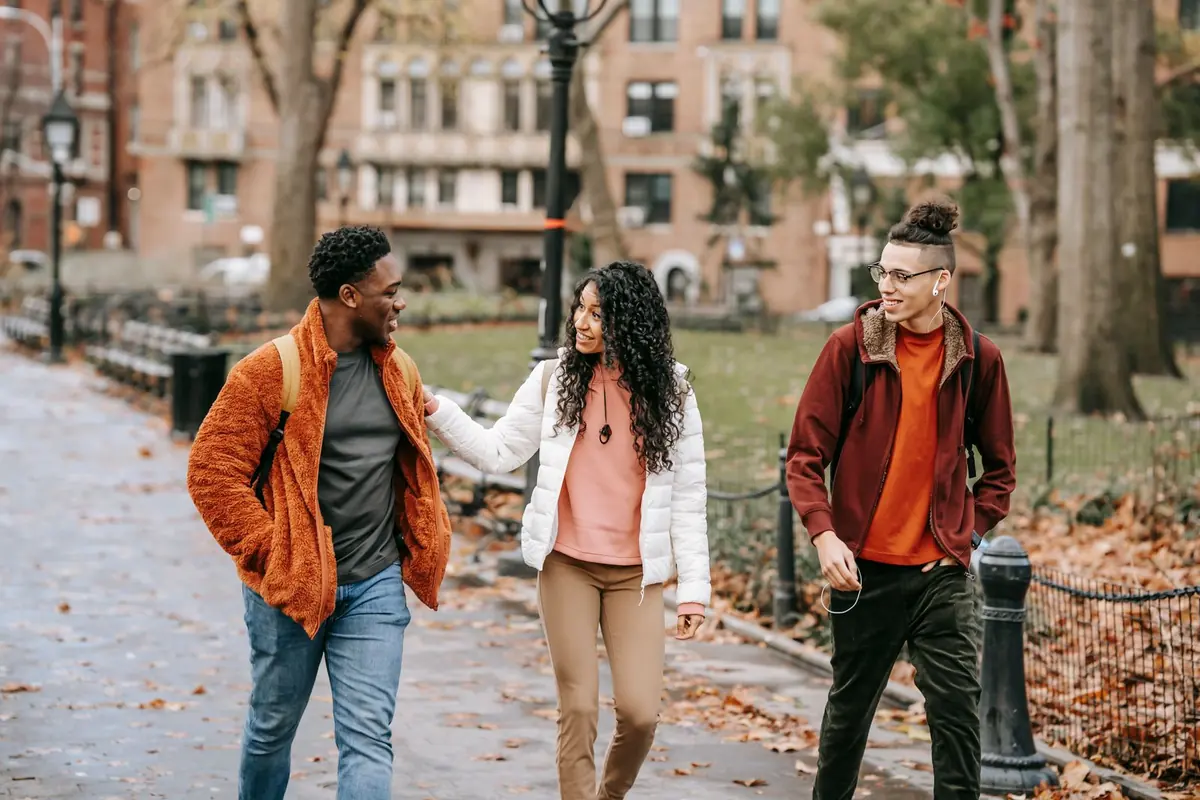 Three friends walking and talking along a tree-lined path in autumn